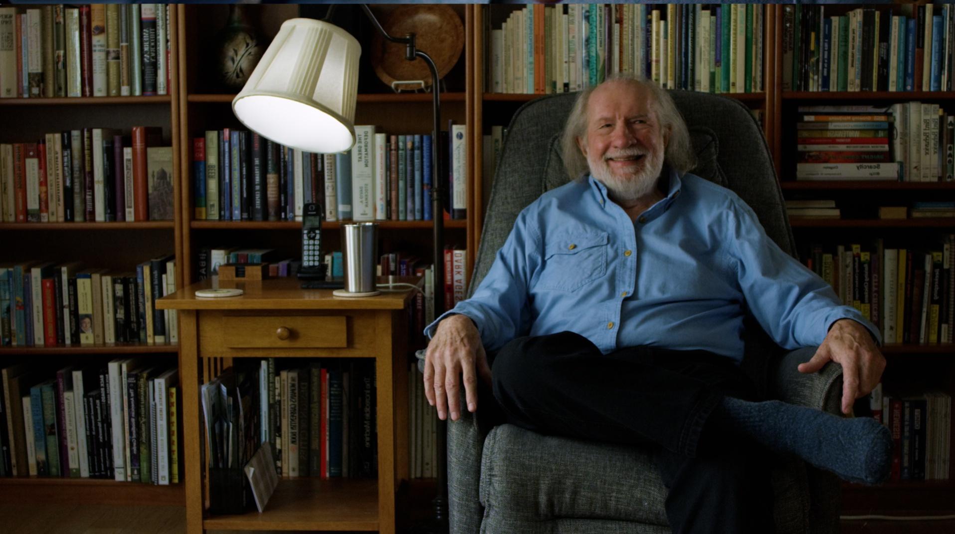 "Man sitting on a chair in a library giving a testimonial. "