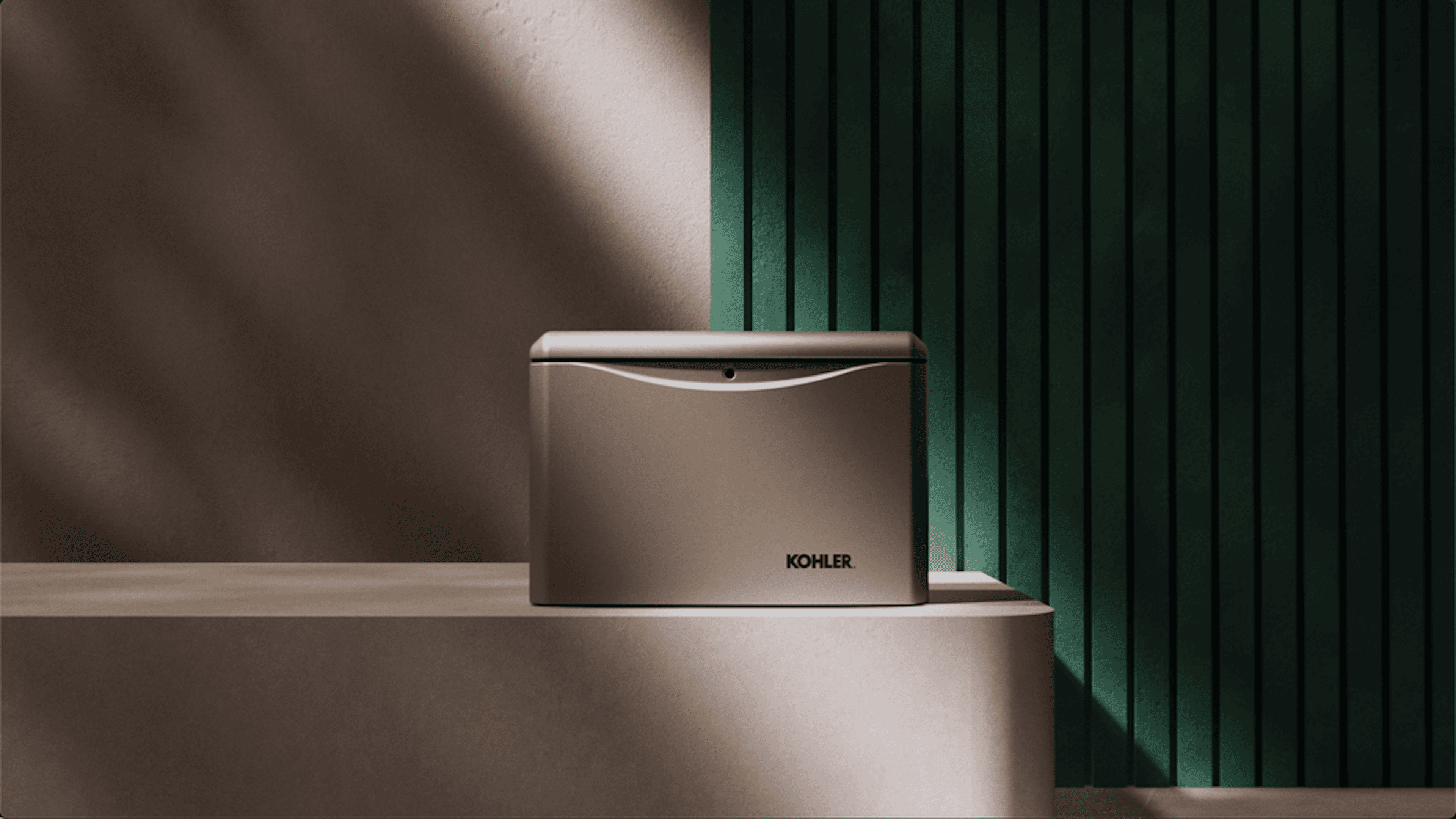 Artful image of grey Kohler home generator on a rectangle platform with rounded corners. Behind the generator is a wall of narrow wood panel painted green. Dramatic lighting casts shadows across the platform and generator