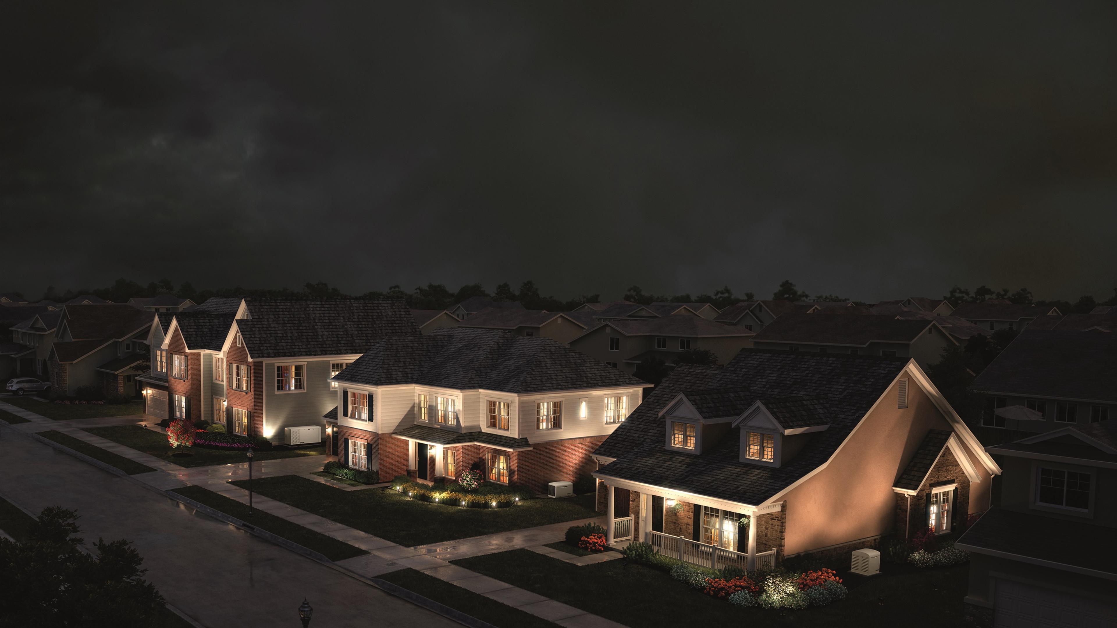 Three houses on a suburban street at night, all illuminated while the rest of the neighborhood is dark.