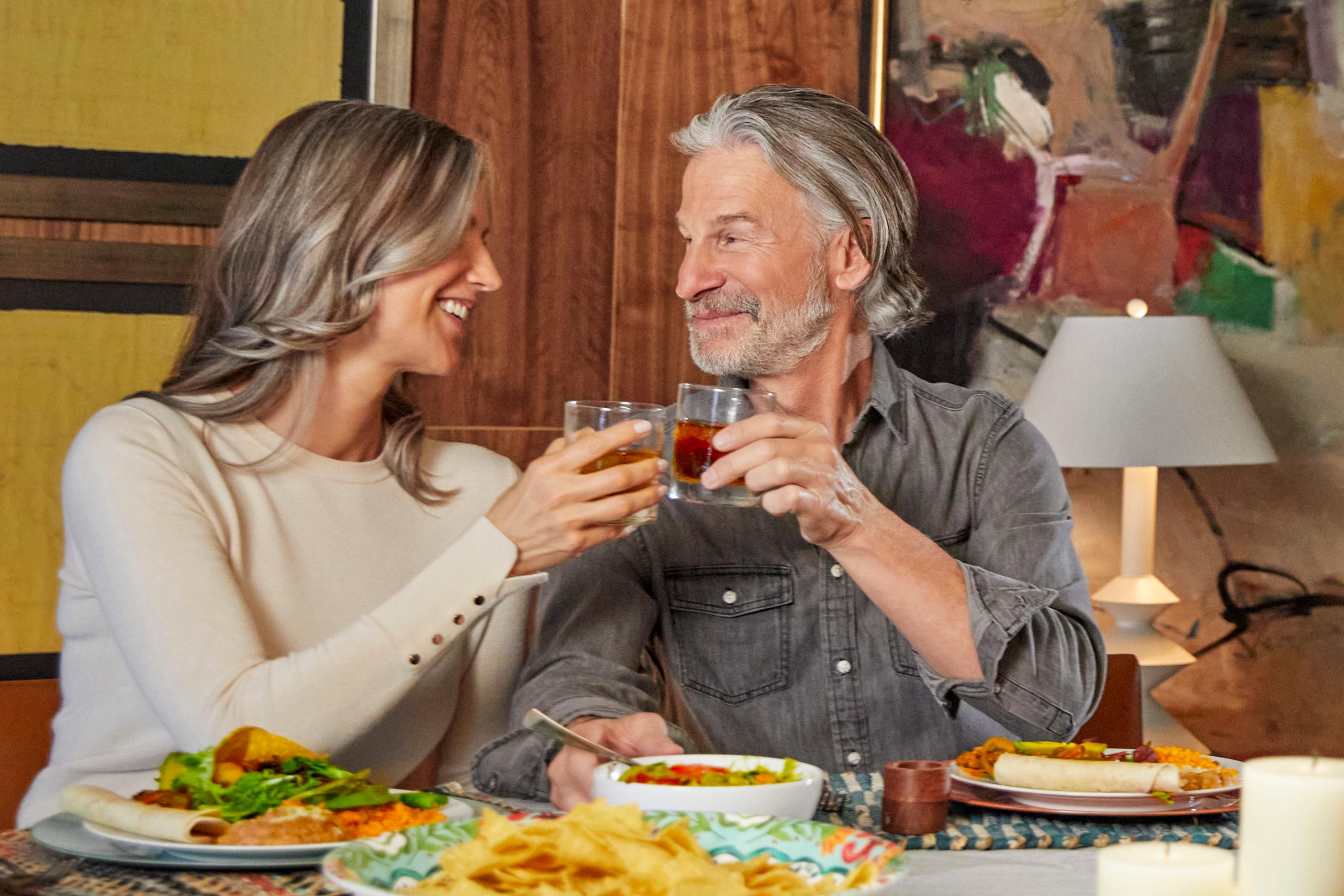 A man and a woman enjoying themselves at a restaurant as they tap their drink glasses together.