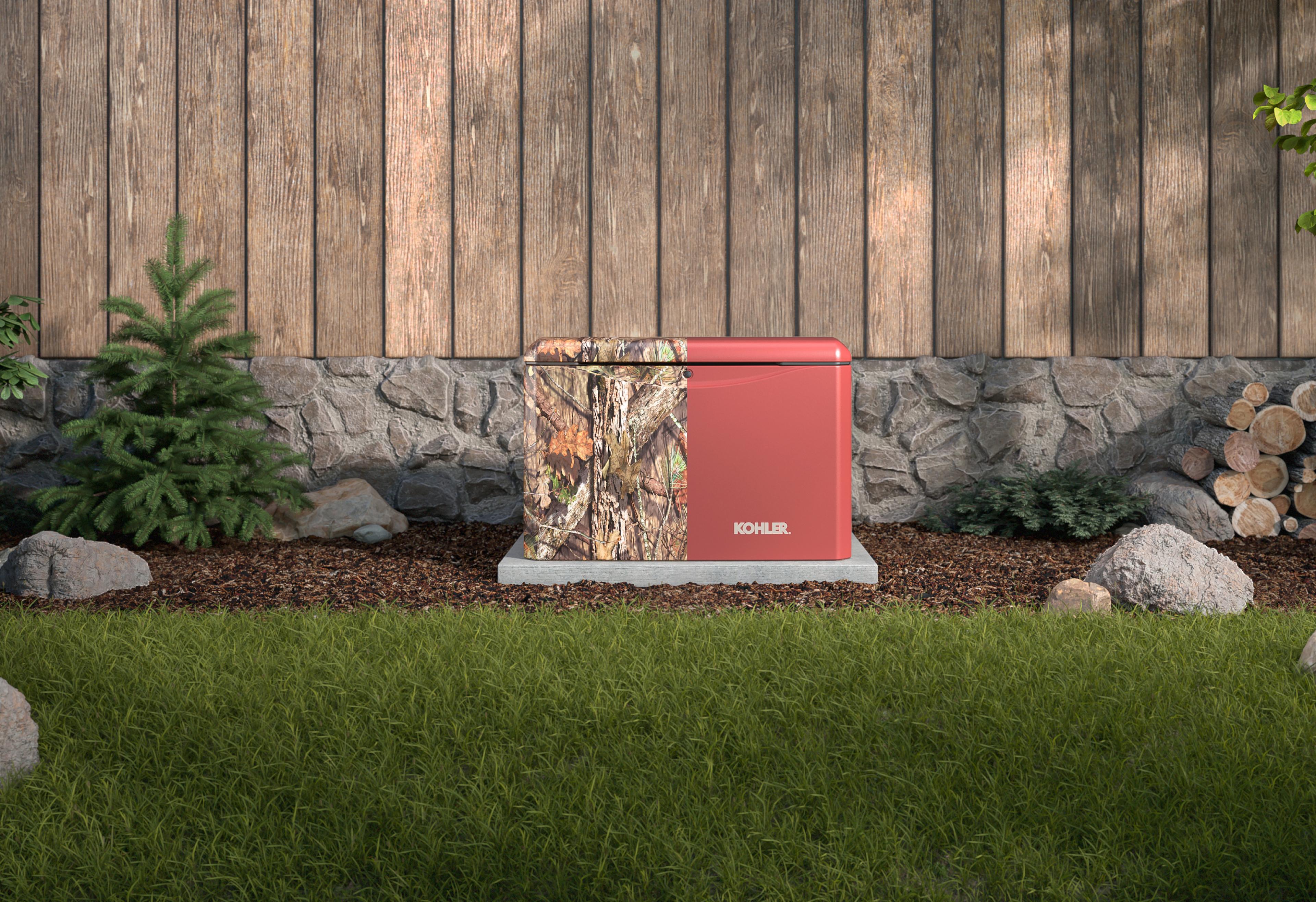 Kohler residential generator with a half camouflage and half red-brick color design, placed outdoors near a wooden fence and stone wall of a residential house.